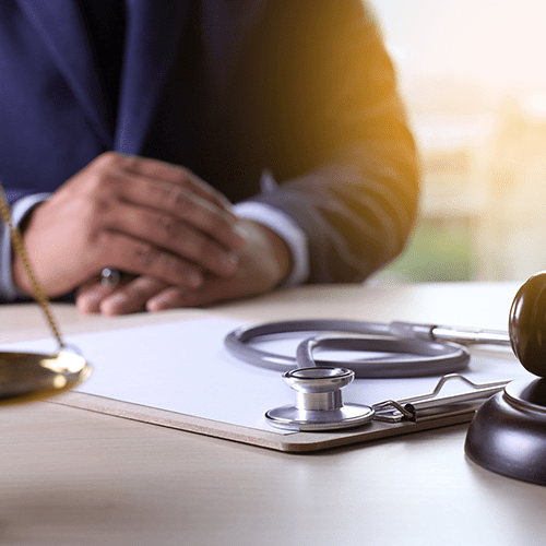 A man sits at a table, which has a gavel, scales of justice, and a stethoscope on top of a clipboard.