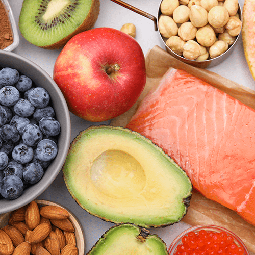 An assortment of foods spred out on a table, including blueberries, kiwi, chickpeas, grapefruit, salmon, avocado, and almonds.