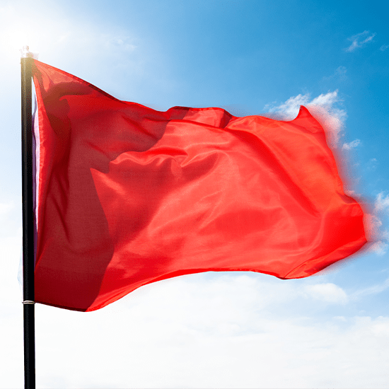 bright red flag flowing in the wind against a cloudy and blue sky