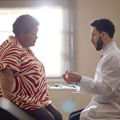 An obese African American woman discussing weight management options with her white, male doctor.