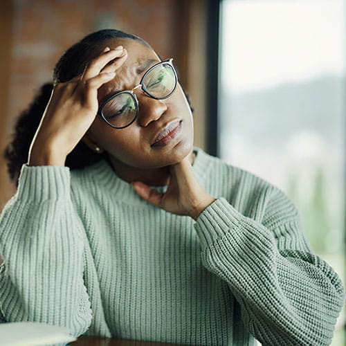 A young African American woman holding her head, looking uncomfortable and concerned.
