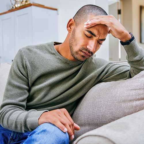 Shot of a young man experiencing a headache while relaxing at home 