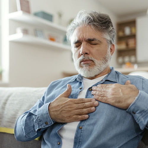 Man holding his chest while sitting on a couch