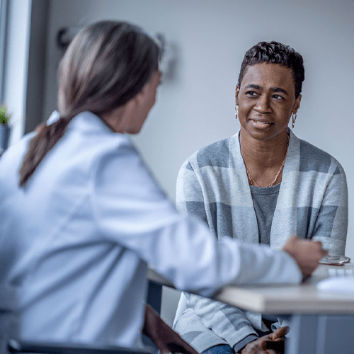 A woman in a gray striped cardigan listens attentively during a consultation with a healthcare provider in a white coat.