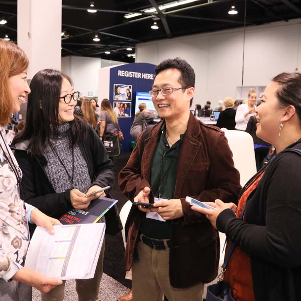 Conference attendees smile while networking on the exhibit hall floor.